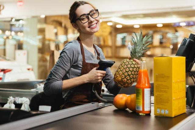 Young woman at a grocery check-out lane preparing to scan a pineapple.