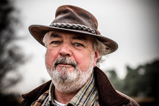 A man in his fifties with white hair and beard and a hat looking directly at us.