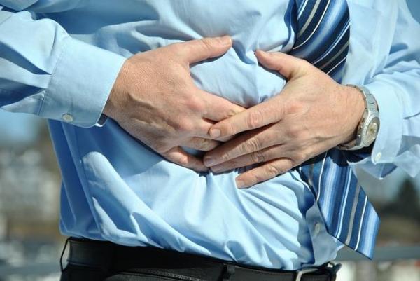 man in dress shirt and tie, holding the side of his abdomen.