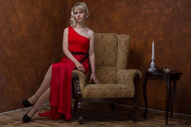 young blonde woman in red dress sitting on the arm of a chair.