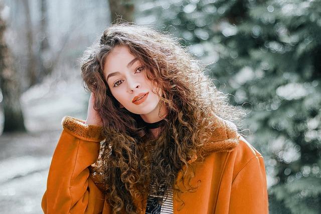 woman in orange coat outside in the winter scratching her head.