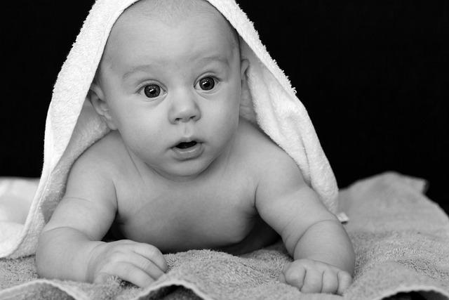 A black and white photo of a baby up on its elbows looking surprised.