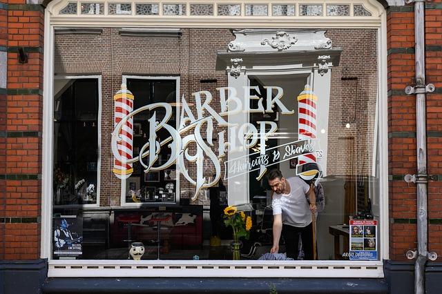 A young man tidying the area immediately outside of his barber shop.