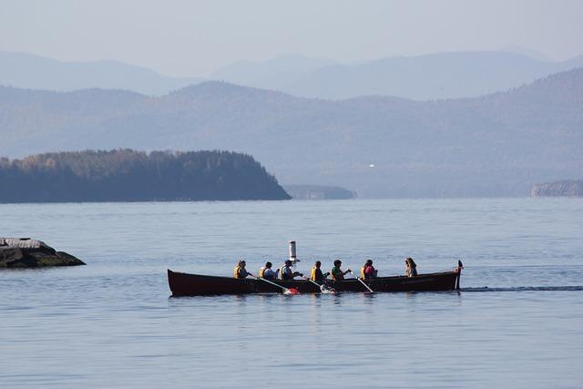 A long boat with 7 people casually rowing, from a distance away.