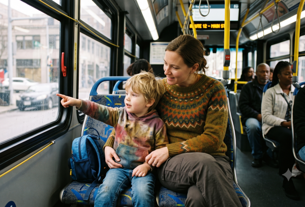 A mom and her young son sitting on a public bus, the son pointing to something out the window.