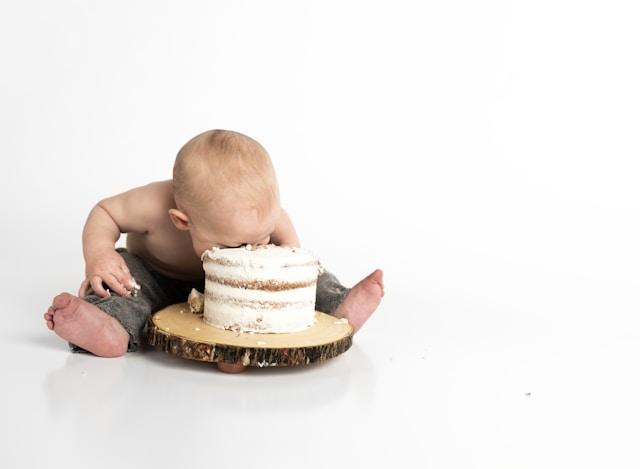 A toddler with his face in a white frosted layer cake, eating whatever he can.