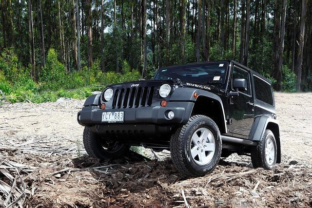 A black jeep parked on an angle on a pile of dirt out in the forest.
