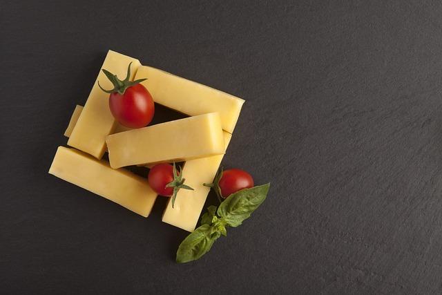 Rectangles of cheddar cheese placed with cherry tomatoes an basil on a dark grey background.