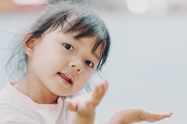 a young girl looking at us with her head to one side and hands raised with a questioning gesture.