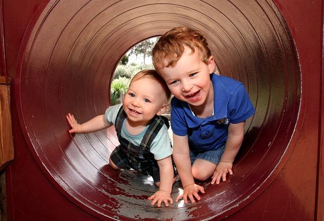 Two young brothers laughing inside a tube at a park.