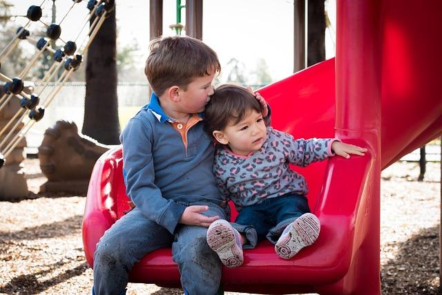 Two boys at the bottom of a slide, the older kissing the top of the head of the smaller.