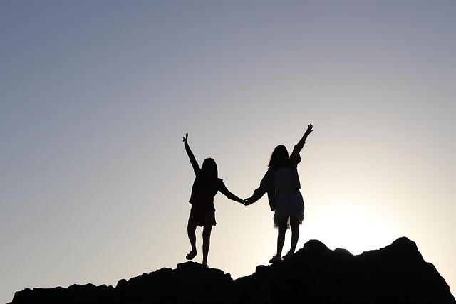 Two young people silhouetted at the top of a mountain with hands raised in triumph and solidarity.