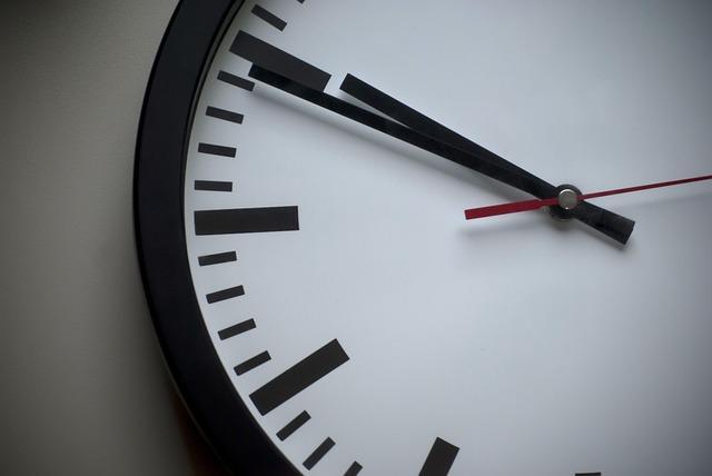 A close-up of an analogue clock with a black rim, a white face, black hands and only lines for the numbers, showing 9:50.