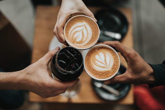 Three friends holding 3 coffees together with the cups all touching.