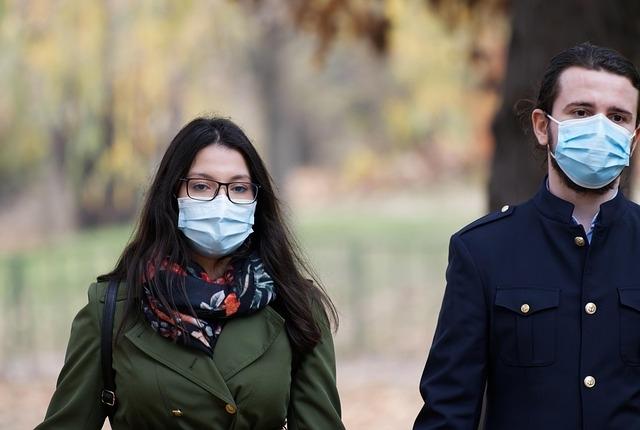 A couple walking outside together, both wearing blue medical masks.