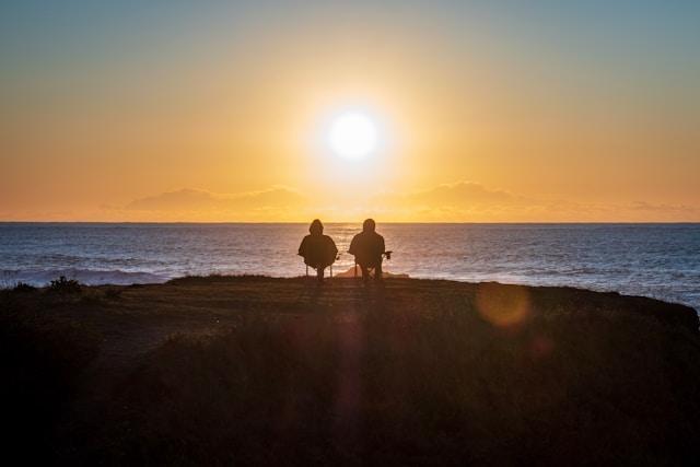 Silhouette of a couple sitting at the side of the ocean watching the sun set.