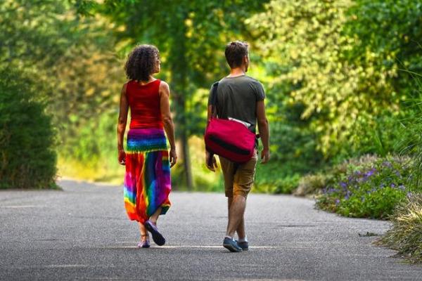 A man and a woman walking away from us along a wide, treed pathway side by side, but a foot apart.