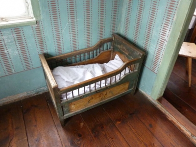 An old wooden crib in the corner of an old home with wood floors and wallpaper from the 1950s.