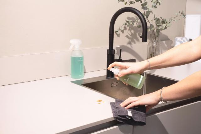 A picture of a woman spraying something on a counter, ready to wipe it down with the cloth in her other hand.
