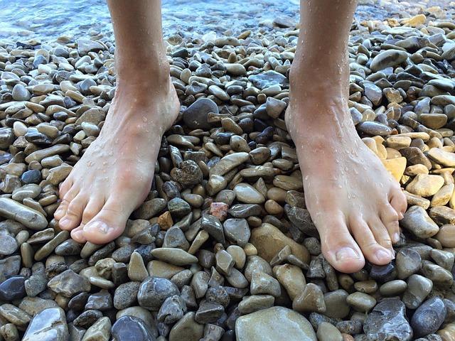 Bare feet standing on rounded pebbly rocks at a beach.