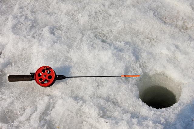 A close-up of a small fishing rod and a hole in the ice. No water is visible.