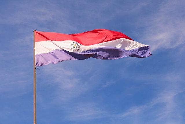 The Paraguay flag flying high against a blue sky.
