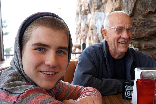 A grandfather and grandson sitting at a cafe table, both are happy.