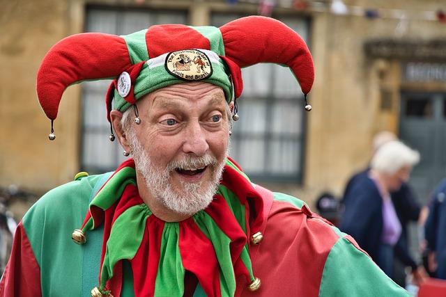 An elderly court jester dressed in red and green with bells and a pleasant smile.