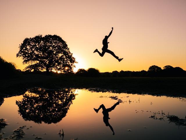 silouette of person jumping across a pond with their reflection below