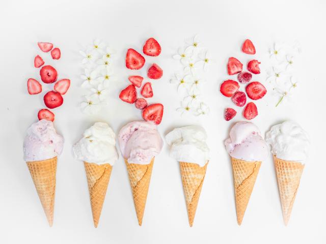 Six ice-cream cones laying flat on a white surface with strawberries and sprinkles above them.
