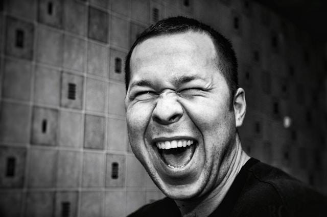 A black and white image of a man laughing with eyes scrunched shut and mouth wide open!