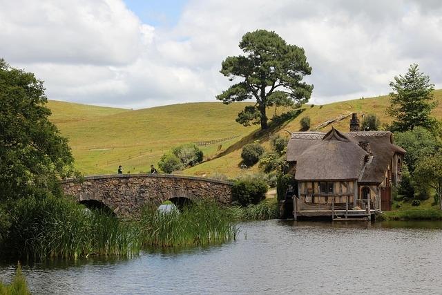 An image of the Shire - looking across a pond to a small house, a stone bridge and gently rolling hills.
