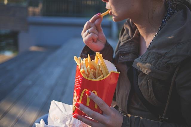A close up of a woman holding a large container of McDonald french fries with one hand and eating one with the other.