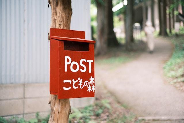 A wooden red mailbox attached to a tree with the label "Post"