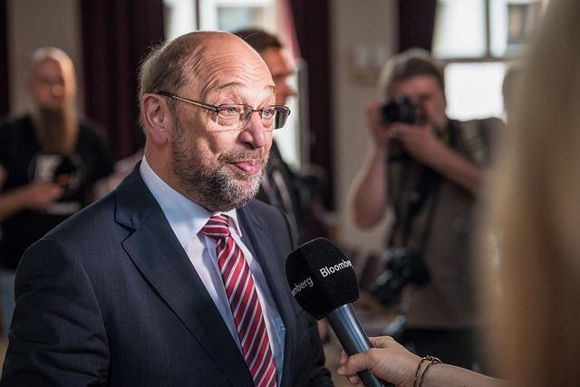 A photo of politician Martin Schulz listening to a question before answering into a mic inside a building.