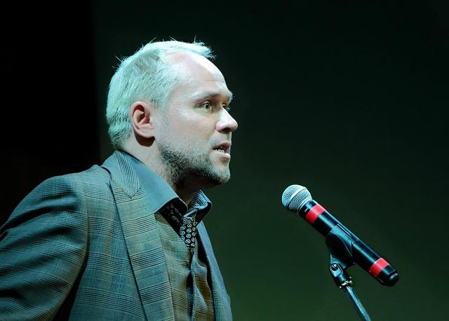 A side view of a man in a suit standing at a microphone on a stand.