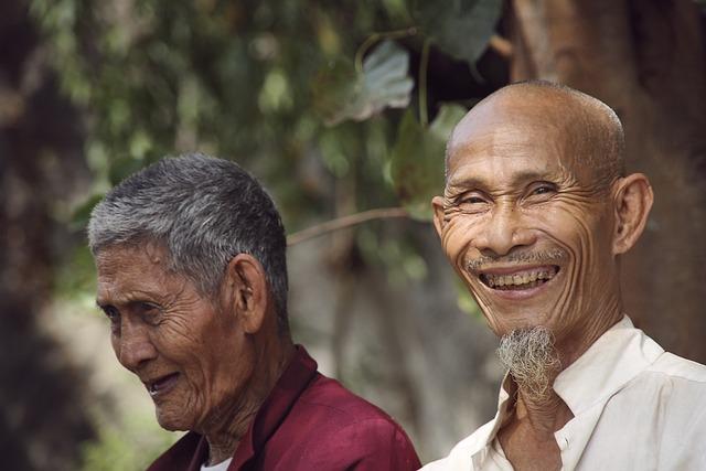 Two south Asian men sitting under a tree laughing.