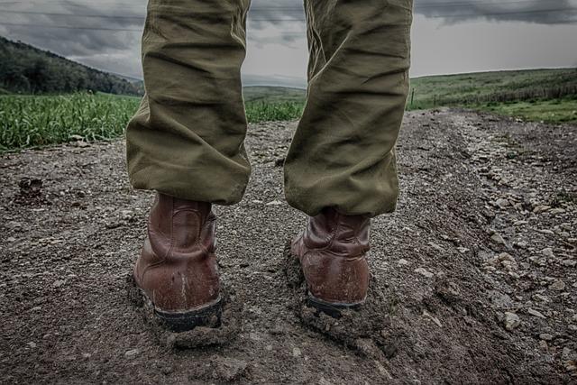 Someone standing in muddy military boots on a dirt road facing away from us.