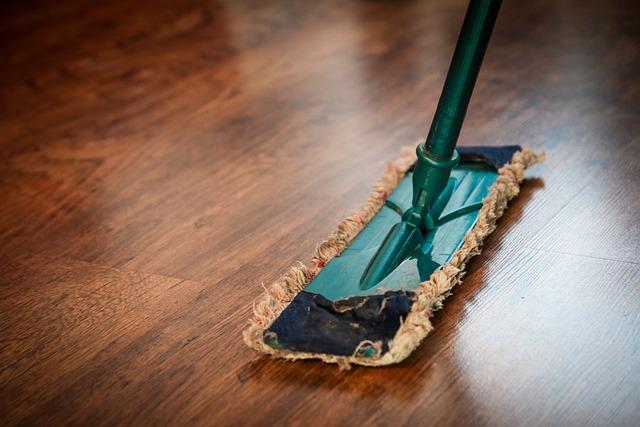 A close-up of a swiffer mop cleaning a golden brown wood-grain laminate floor.