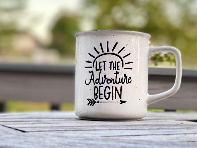A mug on an outdoor table with the slogan "Let the adventure begin"