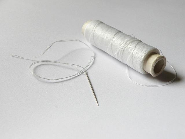 A needle and white thread on a white background.