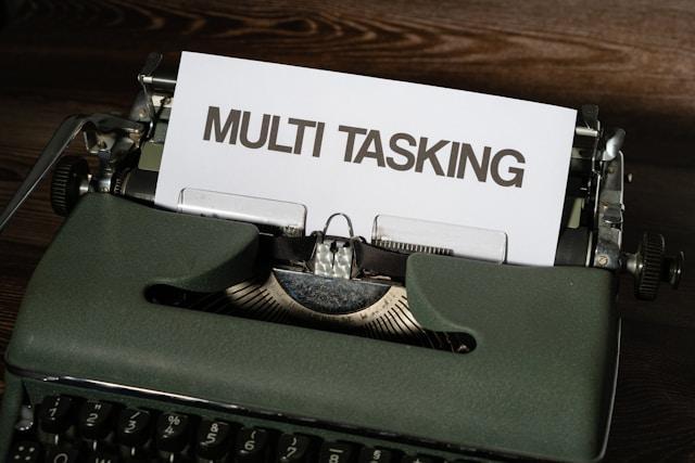 An old-fashioned green typewriter with "multi tasking" written in a large font and all caps on a piece of paper in the machine.