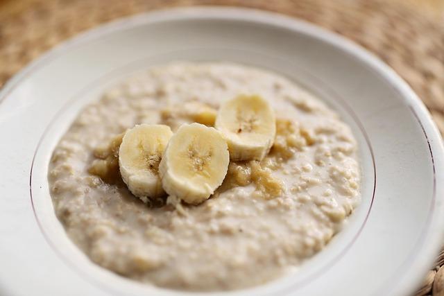 Oatmeal porridge in a white bowl with 3 slices of banana on top.