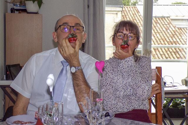 An elderly couple holding a silly fake nose in front of their face.