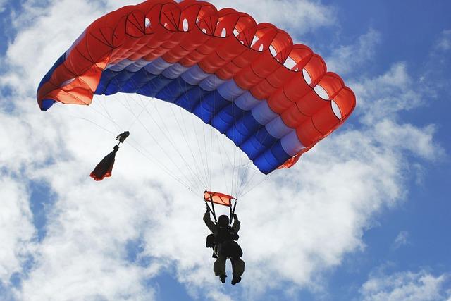 A red and blue parachute against a scattered cloudy blue sky.