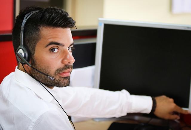 A man in his thirties taking calls at a call centre with headphones on.