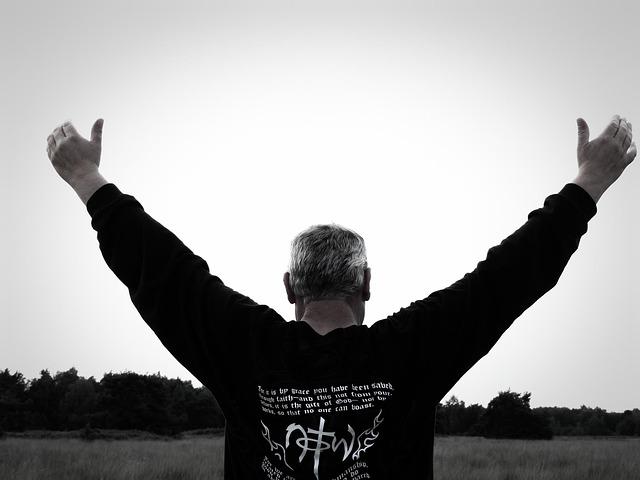 A black and white image of a middle-aged white man from the back, hands raised, head bowed.
