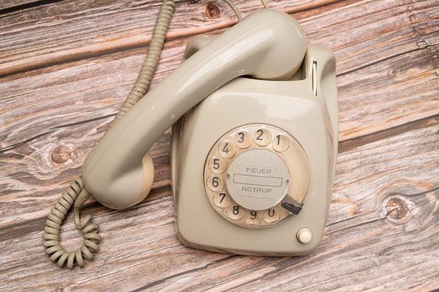 A bone-colored vintage telephone, complete with rotary dial and spiral cord to the handset.