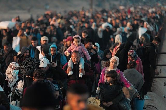 A mass of people, carrying belongings and children, most of them out of focus, with only a few near the front being clear.