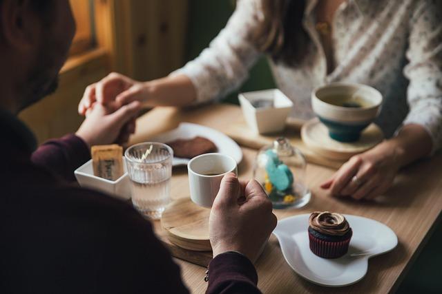 A man and a woman holding hands over a cafe table with coffee, cupcake and more.